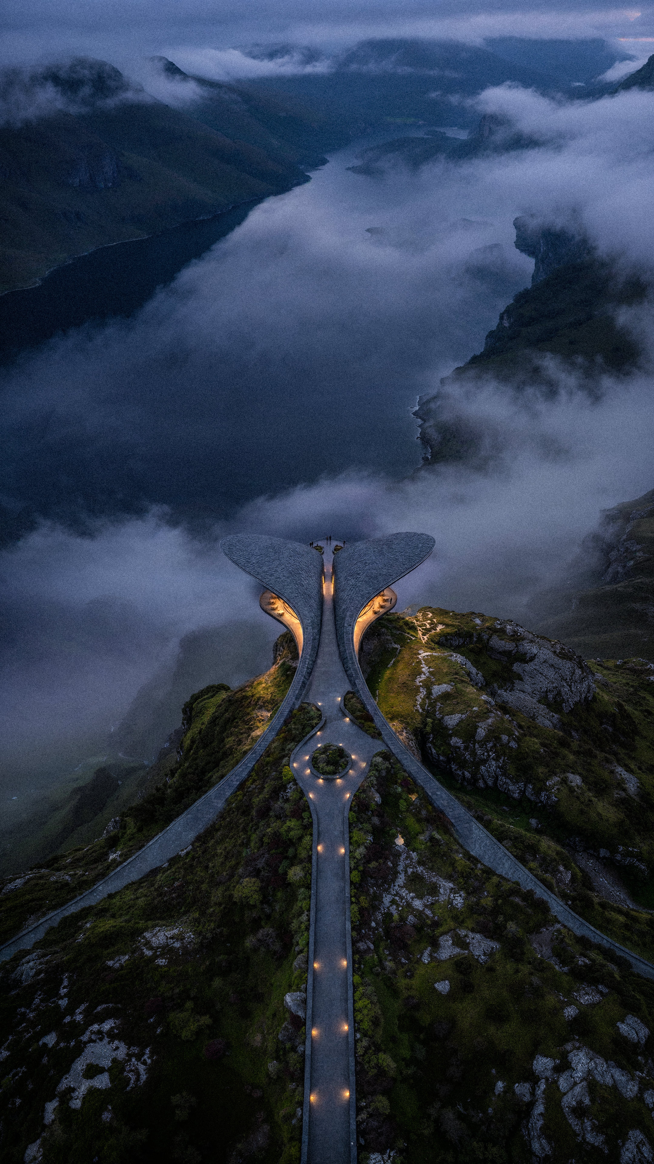 The approach road winding up through low cloud to the lit entrance